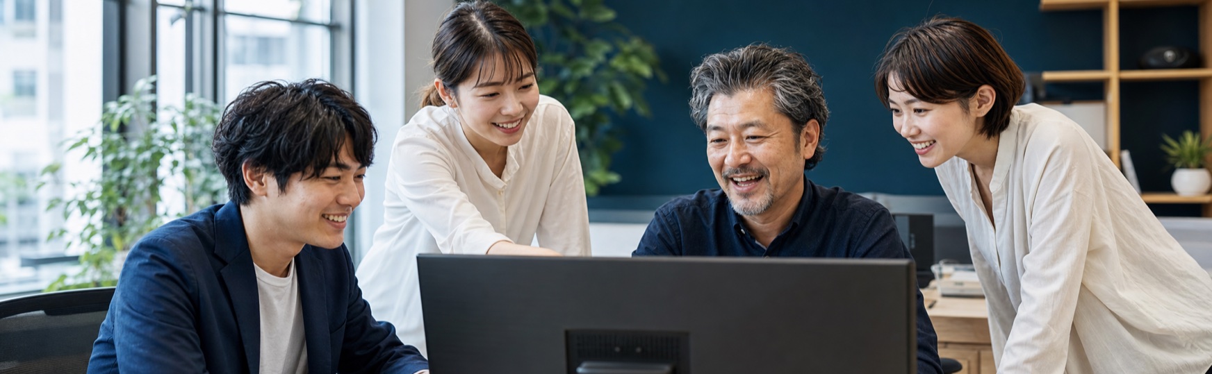 明るいオフィスでモニターを囲み笑顔で議論する日本人チーム